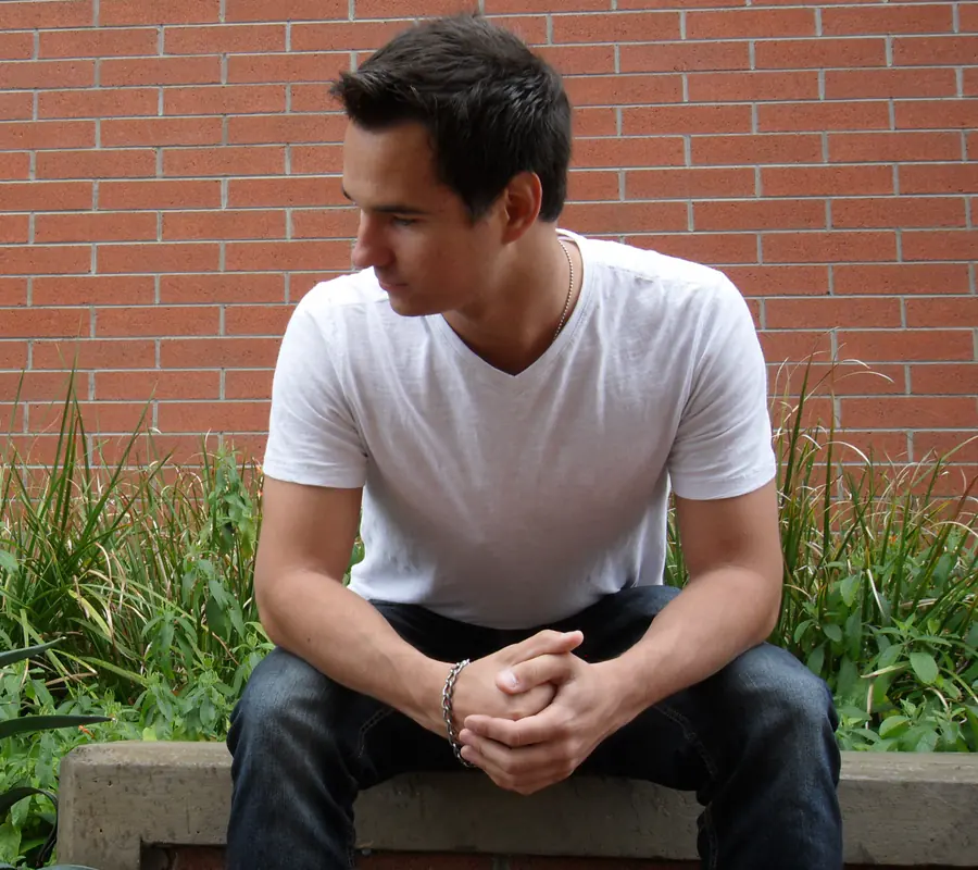Portrait of Roman Godfrey sitting on a stone ledge in front of a red brick wall