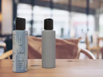 Two dark pump bottles on a wooden table, one carrying the ONE WAY label with the pointing-hand icon
